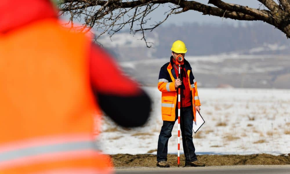 Land surveyor performing fieldwork for ALTA survey along roadside in winter conditions"