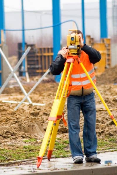 Surveyor using equipment on a large construction site, showing why ALTA land title surveys require weeks of detailed work

