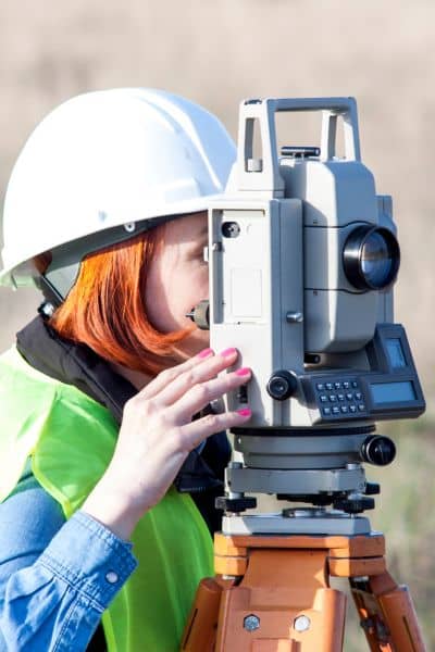 A land surveyor using a total station to measure elevation and map slope conditions during an elevation survey