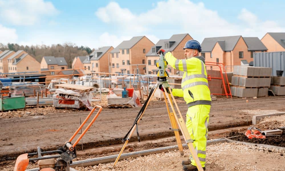 A surveyor uses a total station to perform a construction staking survey on an active new housing development site