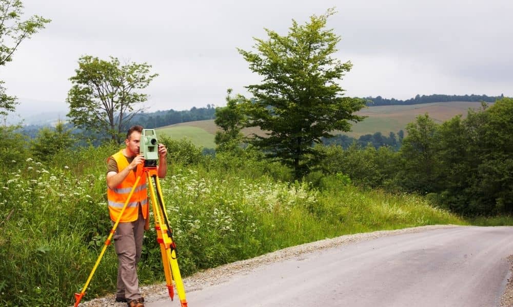 Licensed land surveyor measuring ground elevation during an elevation certificate survey near a residential area