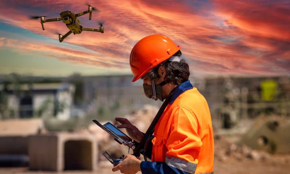 Drone surveying operator reviewing site data on a tablet while capturing aerial images over an active construction project
