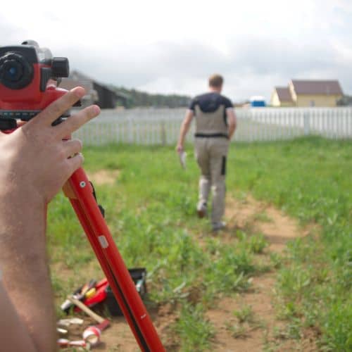 A land surveyor verifying a residential property boundary near a backyard fence using professional surveying equipment