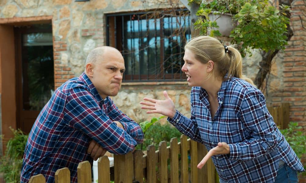 Neighbors arguing over a fence while questioning the property line survey boundary in a residential yard